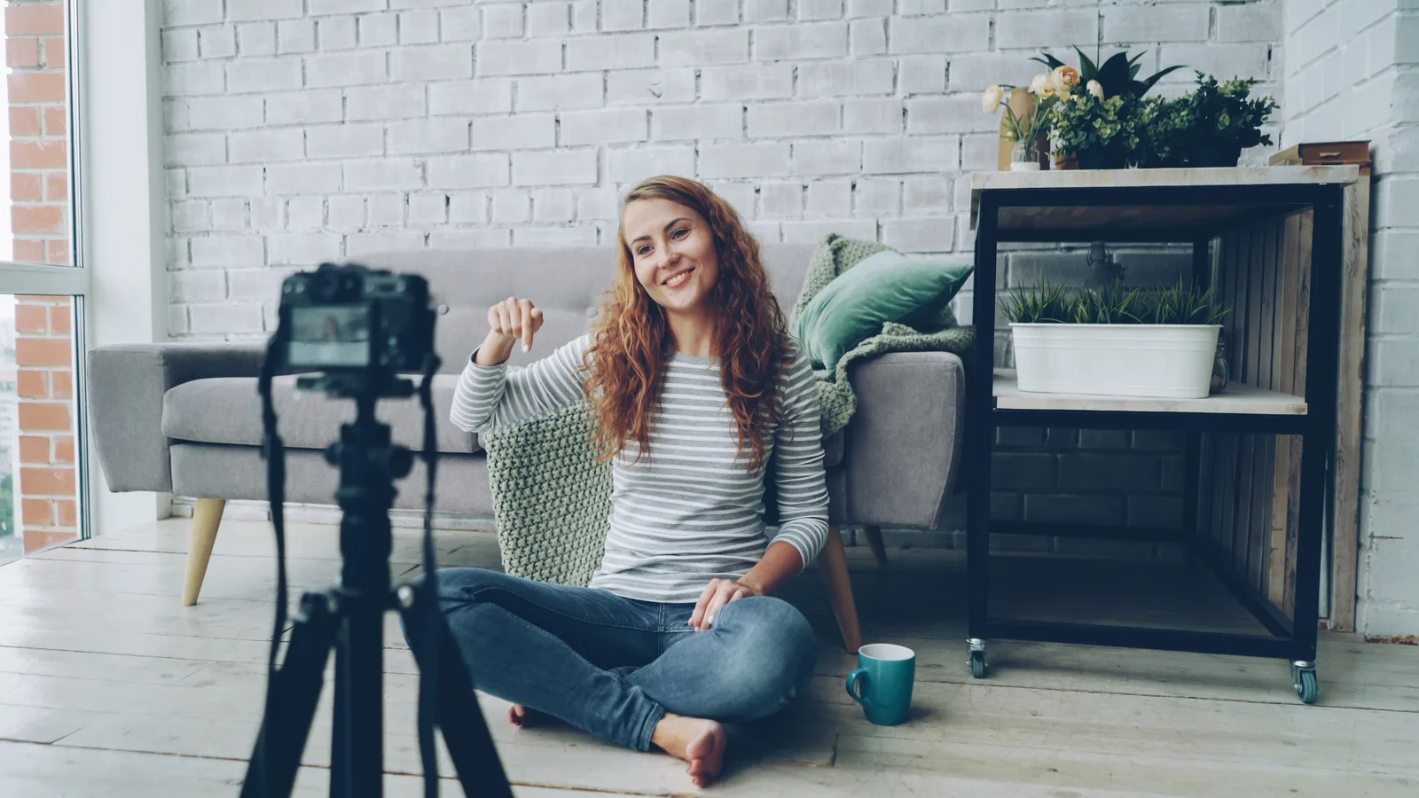 Smiling woman sitting on floor, recording video in cozy room.